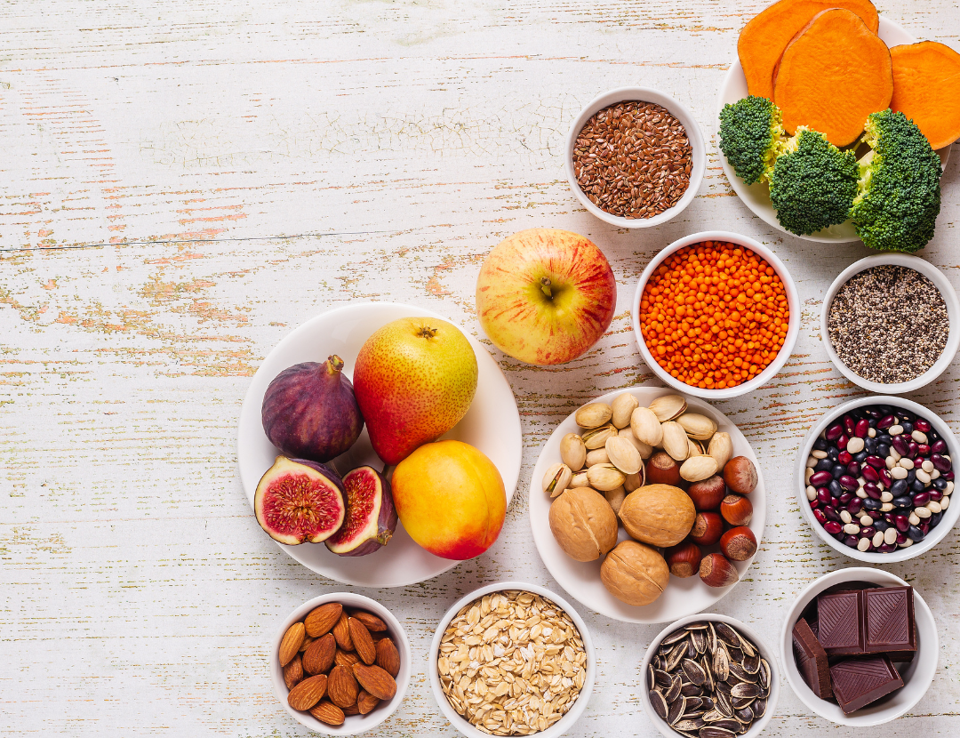 A topdown shot of various nuts, fruits and vegetables on a white wooden table. 