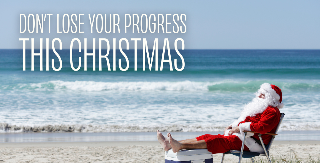 A man on the beach wearing a Santa Claus outfit lying on a chair with his legs resting on a esky