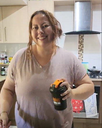 Woman smiling in her kitchen while shaking a Dukes Weight Loss Protein Shaker. 