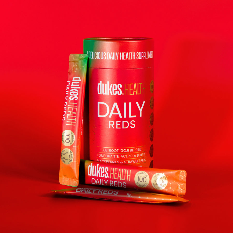 98g 14 Sachet Tube of Dukes Reds Health Supplement on a red background with sachets placed around it. 