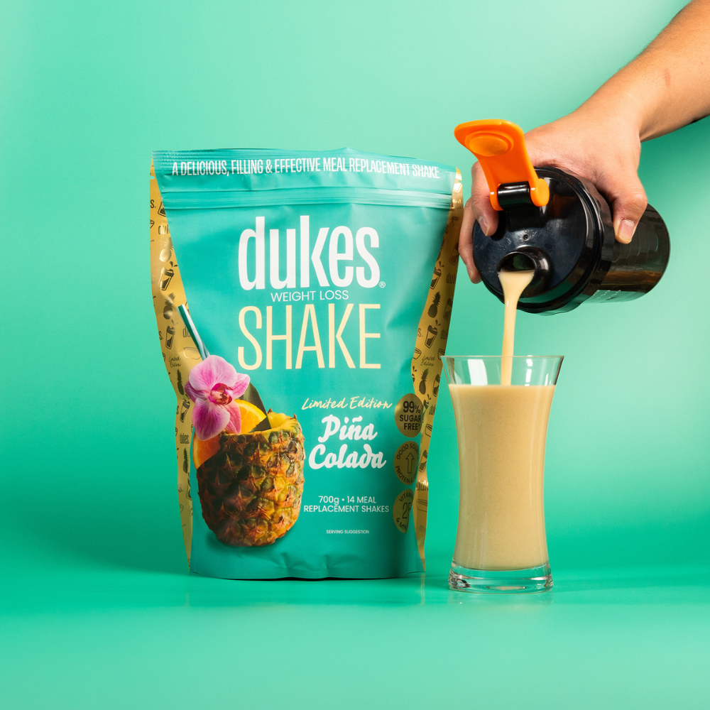 Bag of Dukes Pina Colada Meal Replacement Shake next to a hand pouring the shake into a glass jar