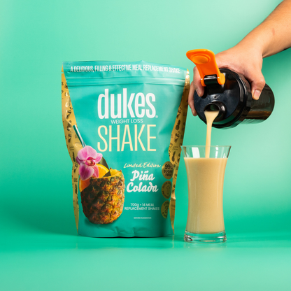 Bag of Dukes Pina Colada Meal Replacement Shake next to a hand pouring the shake into a glass jar